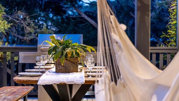 An outdoor dining area with a table set for two, a hammock, and a view of trees. - Njordland -Stunning Oceanside Scandi renovation (Rye)