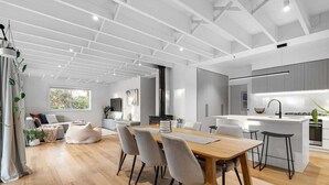 A modern kitchen with a central island, a dining area with a wooden table and chairs, and a living space with a sofa and a coffee table. - Njordland -Stunning Oceanside Scandi renovation (Rye)