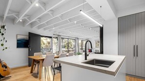 A modern kitchen with a central island, a dining area with chairs, and a large window providing natural light. - Njordland -Stunning Oceanside Scandi renovation (Rye)