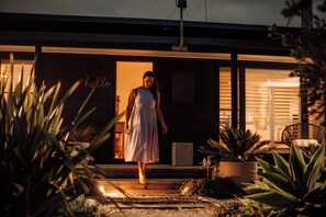 A person walking towards a house with a 'hello' sign on the door, surrounded by plants and a chair. - Quay-Walk to beach Gas Heated Pool, Spa Trampoline (Blairgowrie)