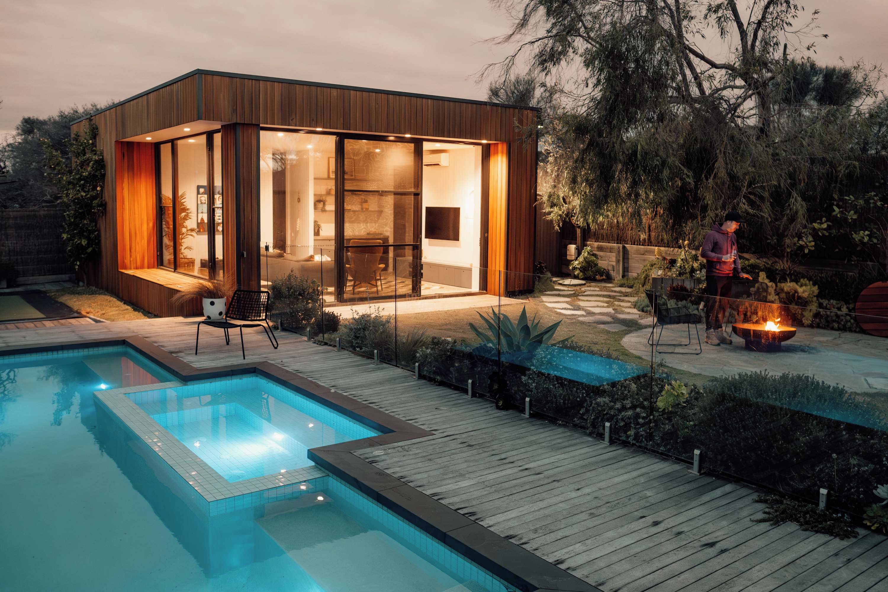 A modern house with a glass-enclosed living area, a wooden deck, and a swimming pool.