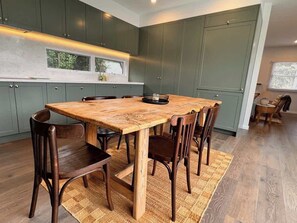 A modern kitchen with dark green cabinets, a wooden dining table, and six chairs. - Safe Haven -walk to beach/shops, full renovation (Sorrento)