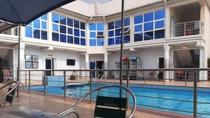Un espace piscine doté d’une structure fermée par des parois en verre, d’une table avec des chaises et d’une rambarde autour de la piscine.