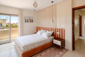 Ein Schlafzimmer mit einem Bett, Nachttischen, einer gemusterten Tagesdecke, einem großen Fenster und Blick auf Gebäude.