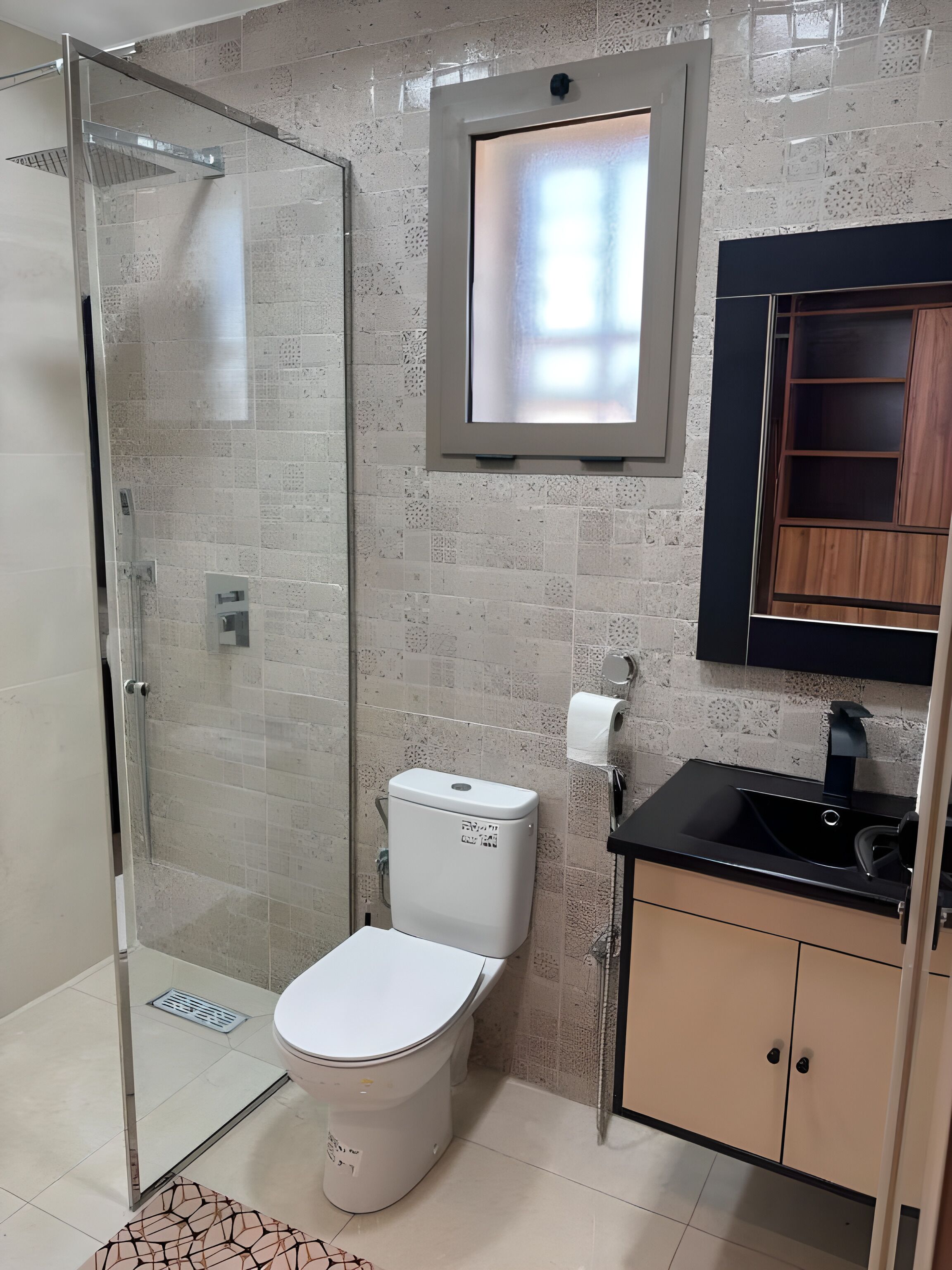 Ein Badezimmer mit Duschkabine aus Glas, Toilette, Waschbecken mit schwarzer Arbeitsplatte und Holzschrank.