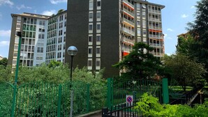 Un edificio residencial de varios pisos con balcones, rodeado de vegetación y una cerca verde.