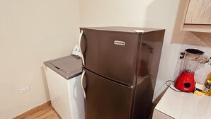 Cocina compacta con un refrigerador negro, lavadora blanca y licuadora roja sobre la encimera.