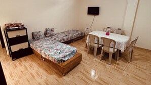 Una habitación con cama, escritorio y sillas, televisor y ventilador de techo.