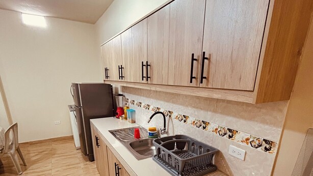 Una cocina con armarios de madera, un refrigerador de acero inoxidable, un lavamanos con grifo y una estufa.