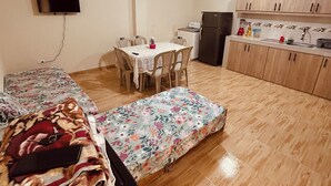 Un espacio habitable compacto con una cama, una mesa de comedor, una kitchenette y un televisor montado en la pared.