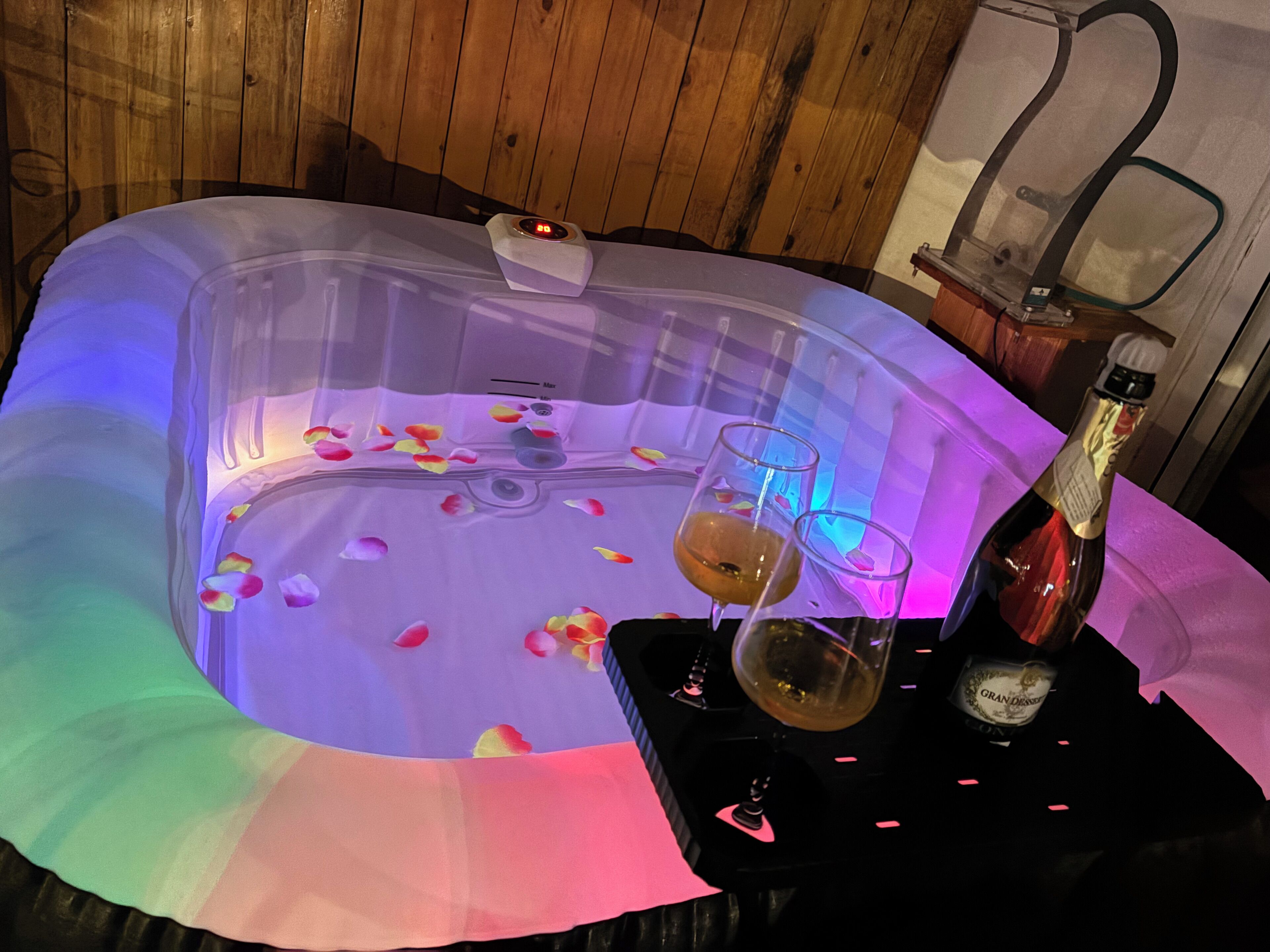 Un bain à remous rempli de pétales de rose, deux verres et une bouteille de champagne.
