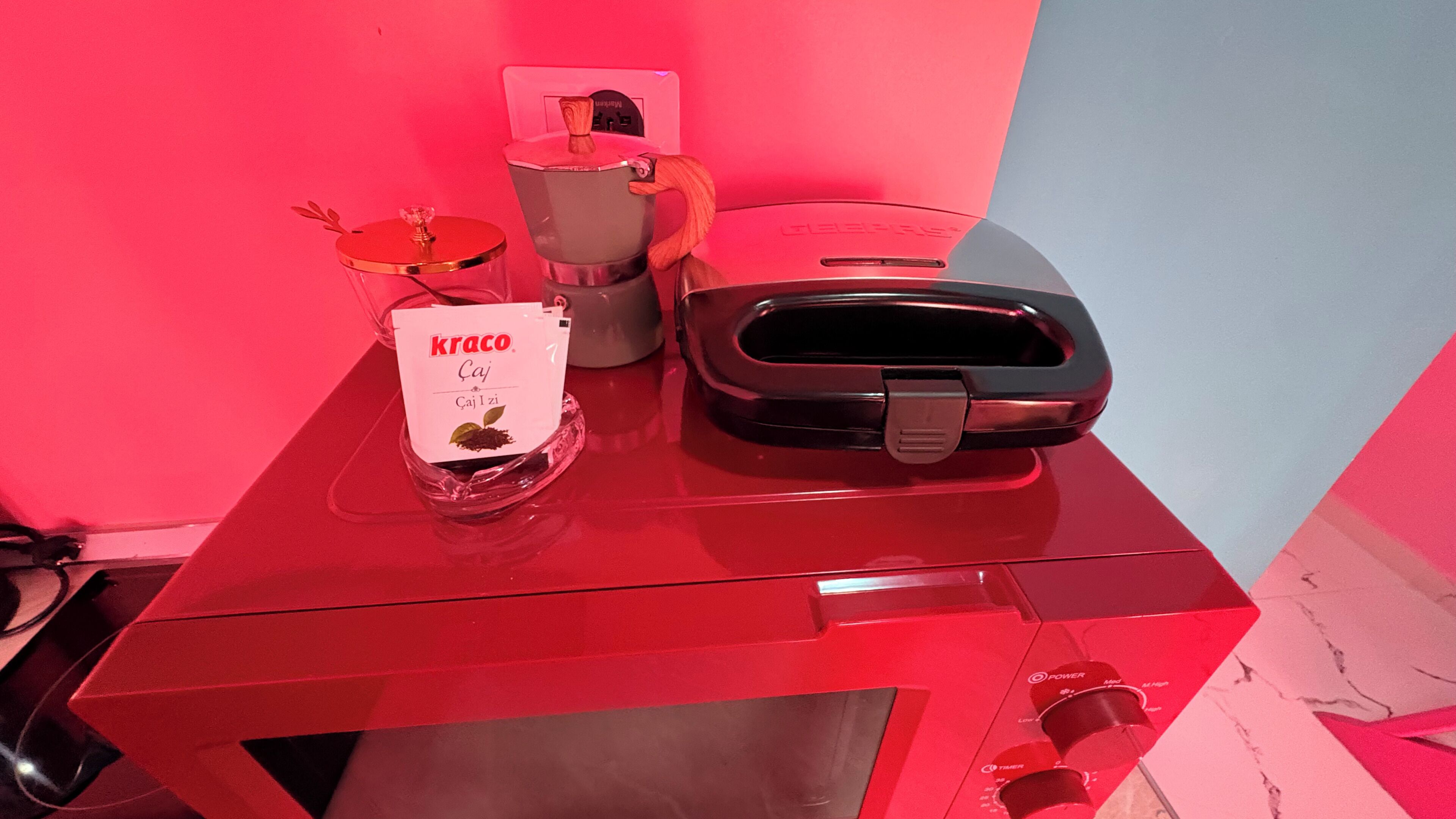 A red table with a coffee machine, a glass jar with a label, and a toaster.