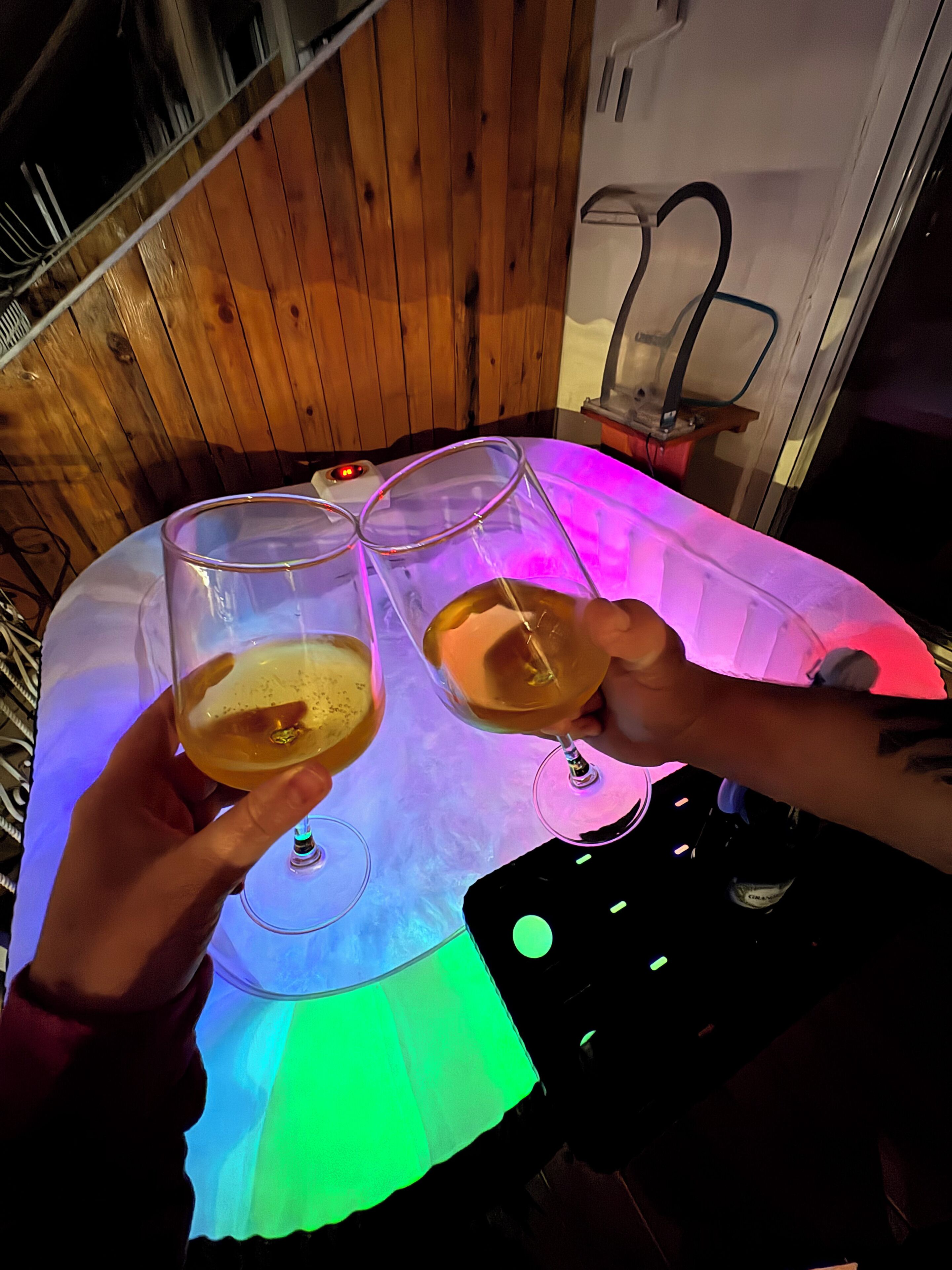 Twee personen houden champagneglazen vast aan een tafel met een kleurrijk lichtspektakel.