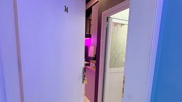 A narrow hallway with a door marked '14' leading to a room with a purple wall and a pink-lit area.