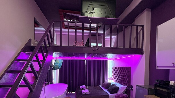 A room with a bunk bed, a white bathtub, a wooden staircase, and a kitchen area. - Romance Apartment (Sarande)