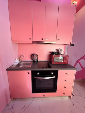 Una cocina rosa con un lavabo, hervidor, tostadora y microondas.
