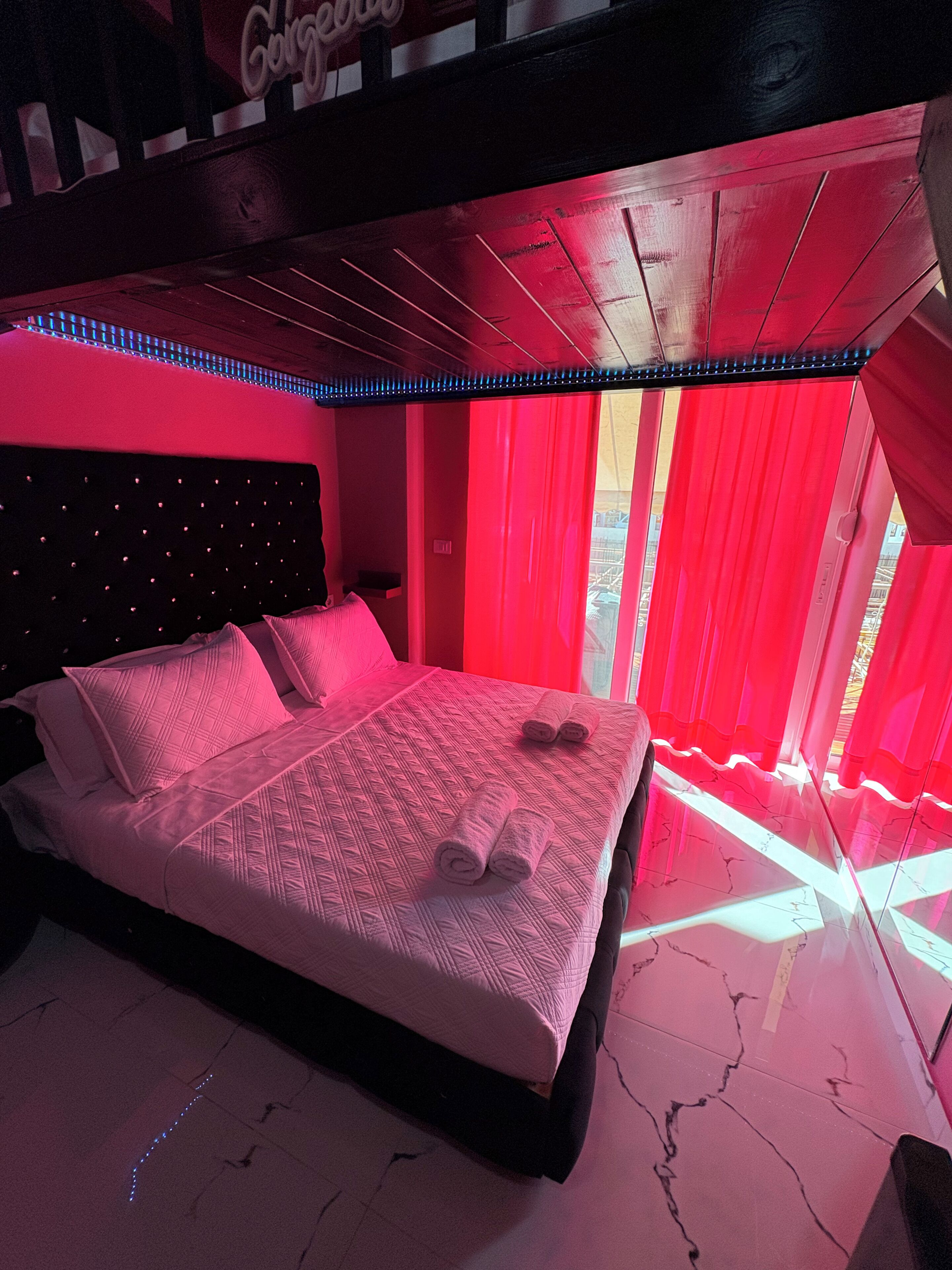 A bedroom with a bed, red curtains, and a neon light strip.
