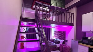 A multi-level room with a staircase, a bed, a sofa, and a kitchen area. - Romance Apartment (Sarande)