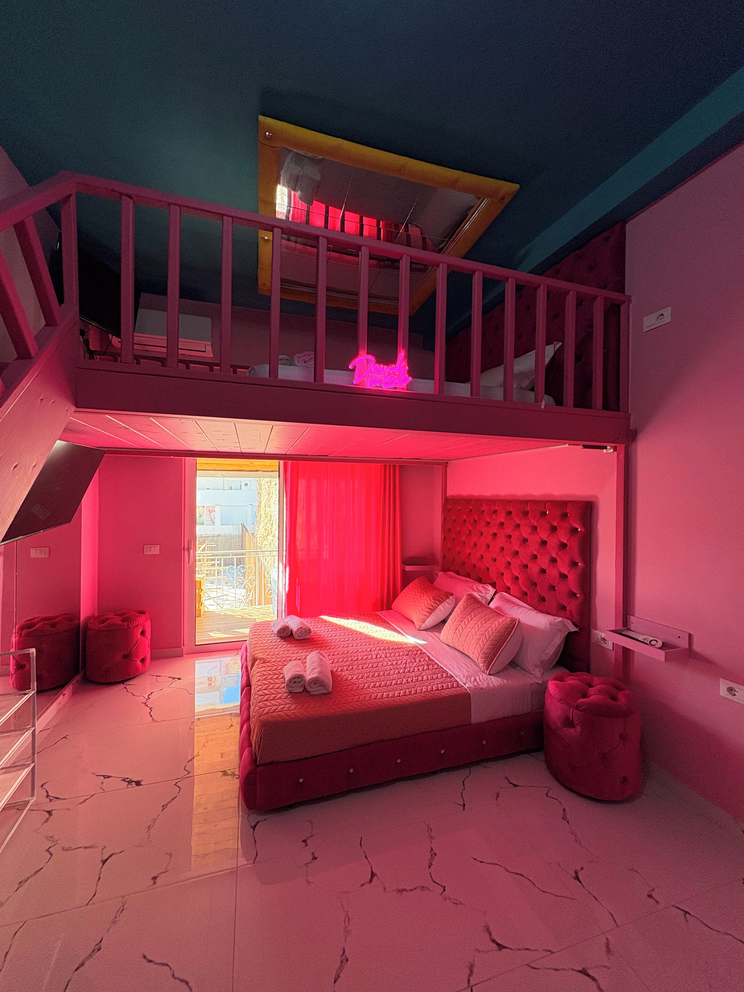 Une chambre avec un lit superposé, un balcon et un panneau lumineux au néon.