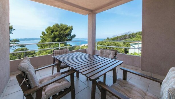 Un balcon avec une table et des chaises en bois, offrant une vue sur la mer et les montagnes.