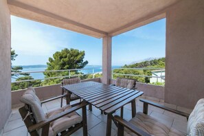 Un balcón con mesa y sillas de madera, que ofrece vistas al mar y a las montañas.