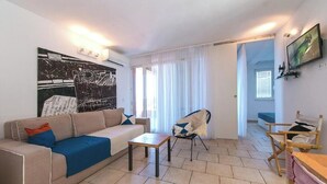 Ein Wohnzimmer mit einer Couch, einem Couchtisch und einem Sessel. An der Wand hängt ein Gemälde und ein Fernseher ist angebracht.