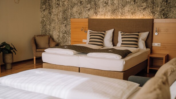 A neatly made bed with a wooden headboard, two pillows, and a bedside table with a lamp. - Auszeit Hotel (Sankt Lambrecht)