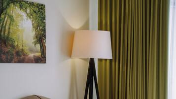 Habitación de hotel con cama, mesita de noche, lámpara y un cuadro de una escena boscosa.