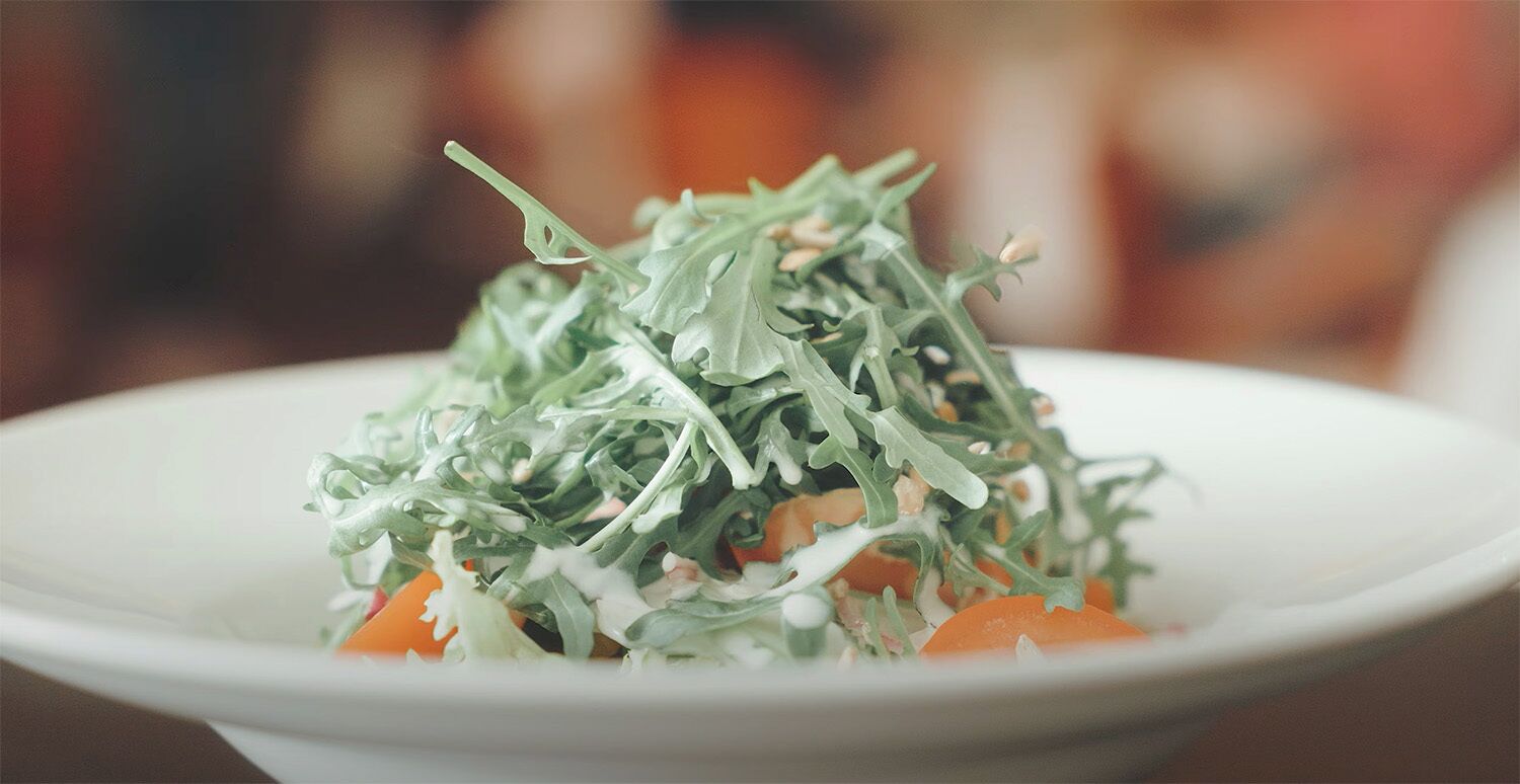 A white plate with a salad consisting of arugula and carrots.