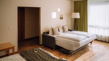 A hotel room with a bed, a sofa, a small table, and a door leading to another room.