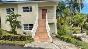 A two-story building with a staircase leading to the entrance, surrounded by lush greenery and palm trees. - 2nd Visit Guaranteed (Sosúa)