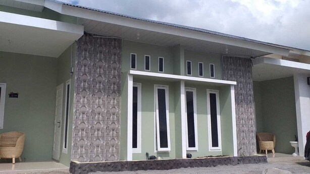 A building with a green facade, a covered porch area, and two wicker chairs outside. - Pintu Waluh Homestay (Takengon)