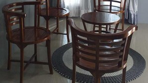 A dining area with a round table and four chairs, a mirror on the wall, and three windows with curtains. - Pintu Waluh Homestay (Takengon)