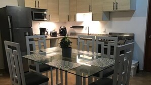 Eine kompakte Küche mit einem Glastisch, weißen Stühlen, einem Kühlschrank, einer Mikrowelle, einem Herd und einer Kaffeemaschine.