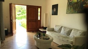 Ein Wohnzimmer mit einem Rattan-Sofa, einem Couchtisch und einer Tür, die in einen Garten führt.