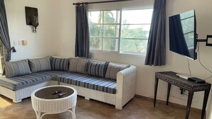 A living room with a sectional sofa, a round coffee table, a flat-screen TV, and a window with curtains. - Villa Belle Amour (Sosúa)