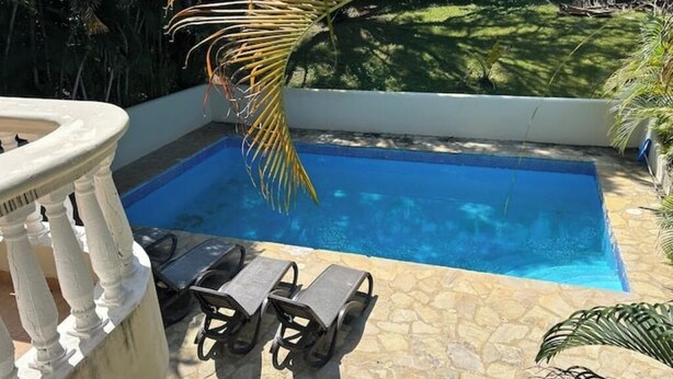 A swimming pool with lounge chairs and a stone-tiled deck. - Villa Belle Amour (Sosúa)