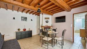 Un comedor con techo de madera, una mesa redonda y cuatro sillas. Hay un televisor montado en la pared y una chimenea con repisa.