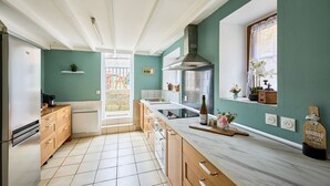 Una cocina con armarios de madera, una campana extractora de acero inoxidable, una encimera de mármol y un ventanal con vistas al exterior.