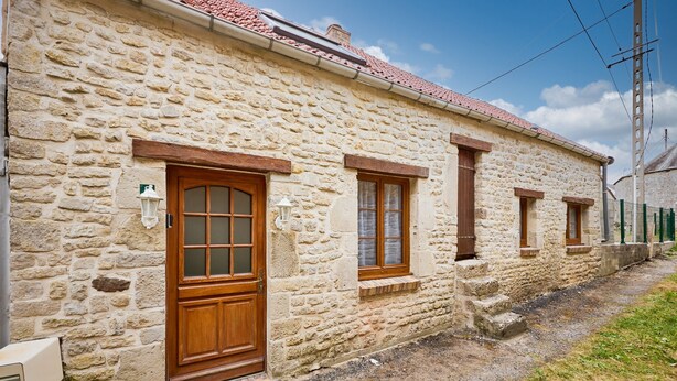 Un edificio de piedra con puerta y ventanas de madera, un pequeño porche y un techo inclinado.