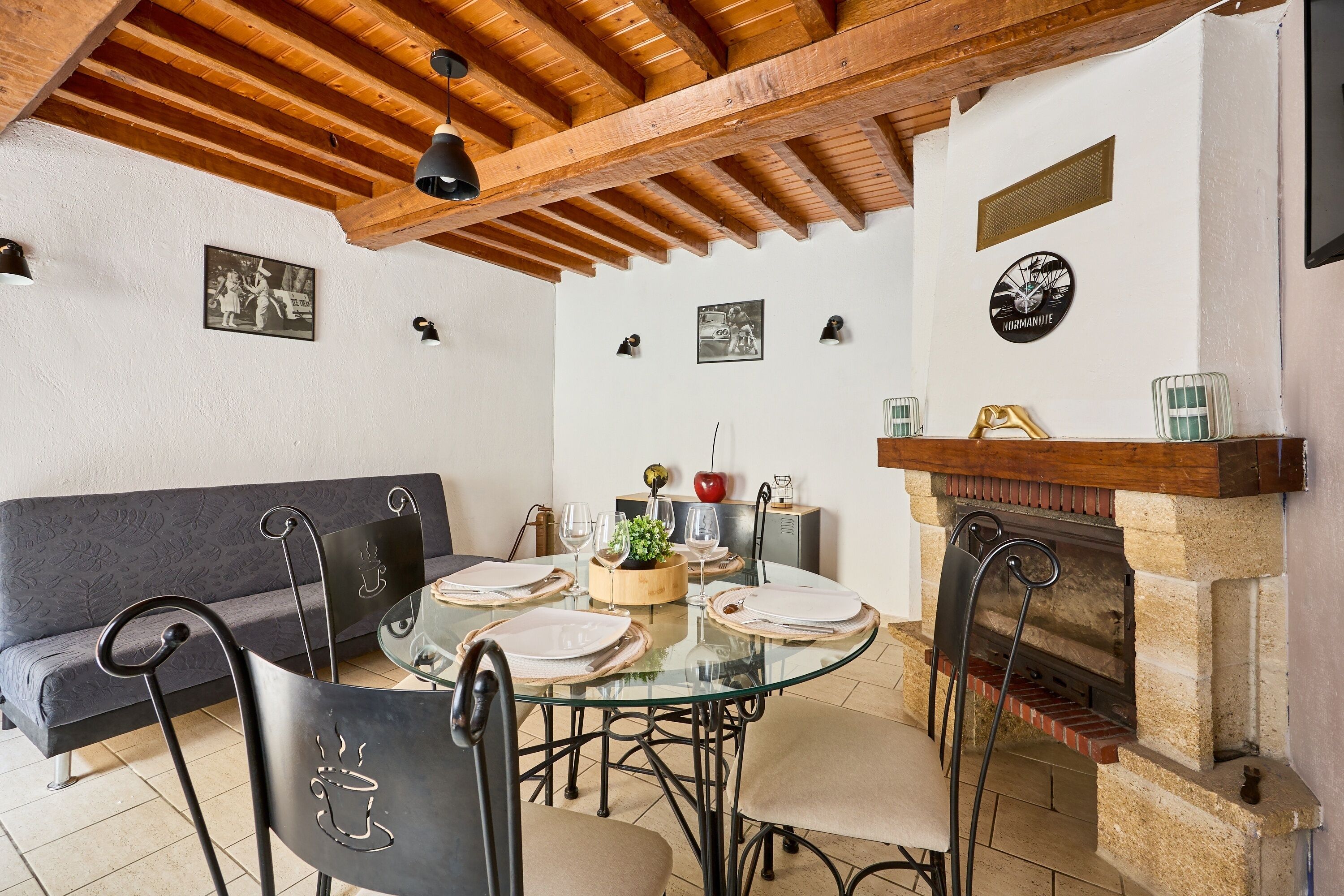 Een eetruimte met een glazen tafel, metalen stoelen, een houten plafond en een schouw van baksteen.