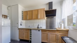 Cocina compacta con armarios de madera, extractor de acero inoxidable, lavavajillas y ventana con vistas al exterior.
