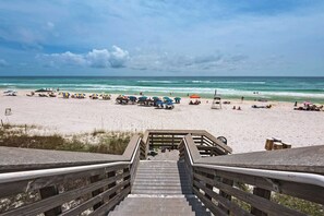 A wooden staircase leading to a beach with umbrellas and beach chairs.