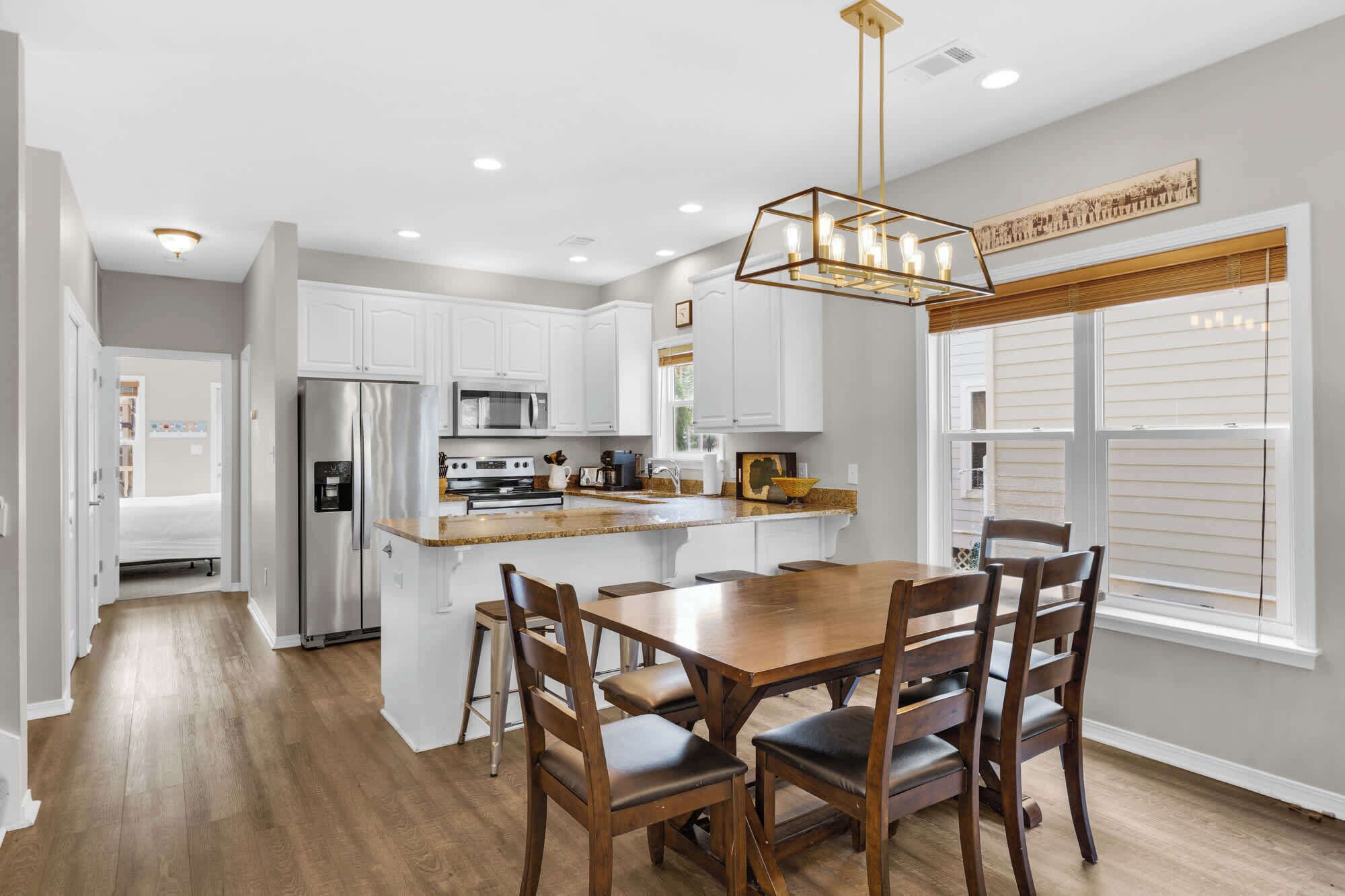A modern kitchen with white cabinets, stainless steel appliances, a wooden dining table, and a pendant light.