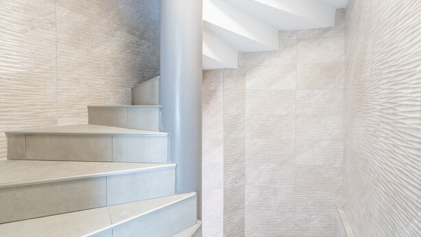 Un escalier moderne au design minimaliste, avec un mur de couleur claire à la texture discrète et un plafond blanc et épuré.