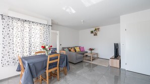 Un salon moderne comprenant un coin repas, un canapé gris et un téléviseur posé sur un meuble en bois.