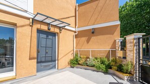Un bâtiment moderne avec une porte grise, un espace extérieur abrité et un petit jardin avec des plantes.
