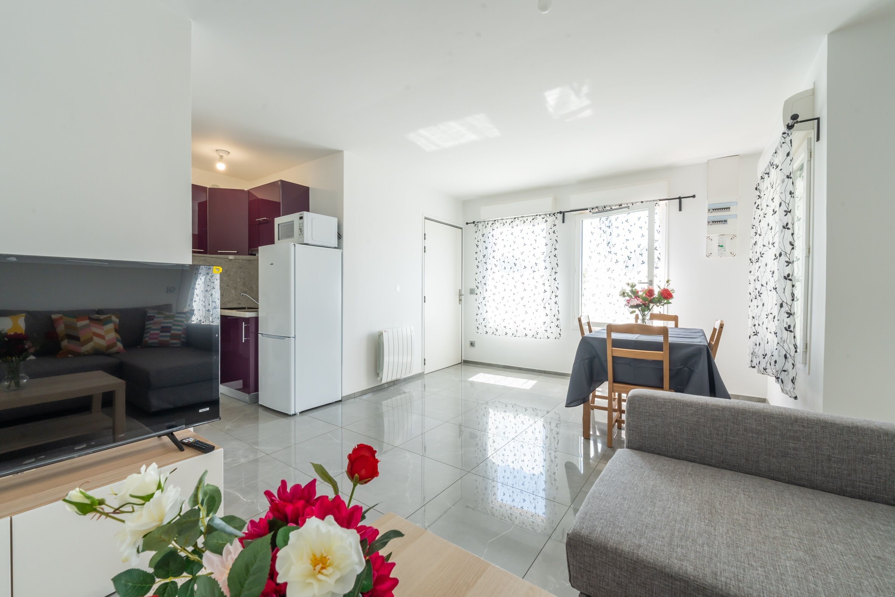 A modern living room with a flat-screen TV, a sofa, and a dining area with a table and chairs.