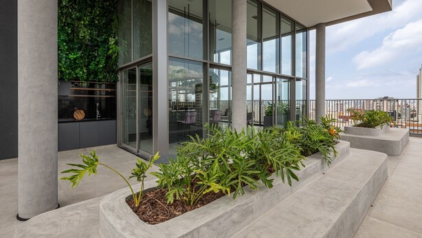 A modern building with large glass windows, a balcony with outdoor seating, and a vertical garden on the left.