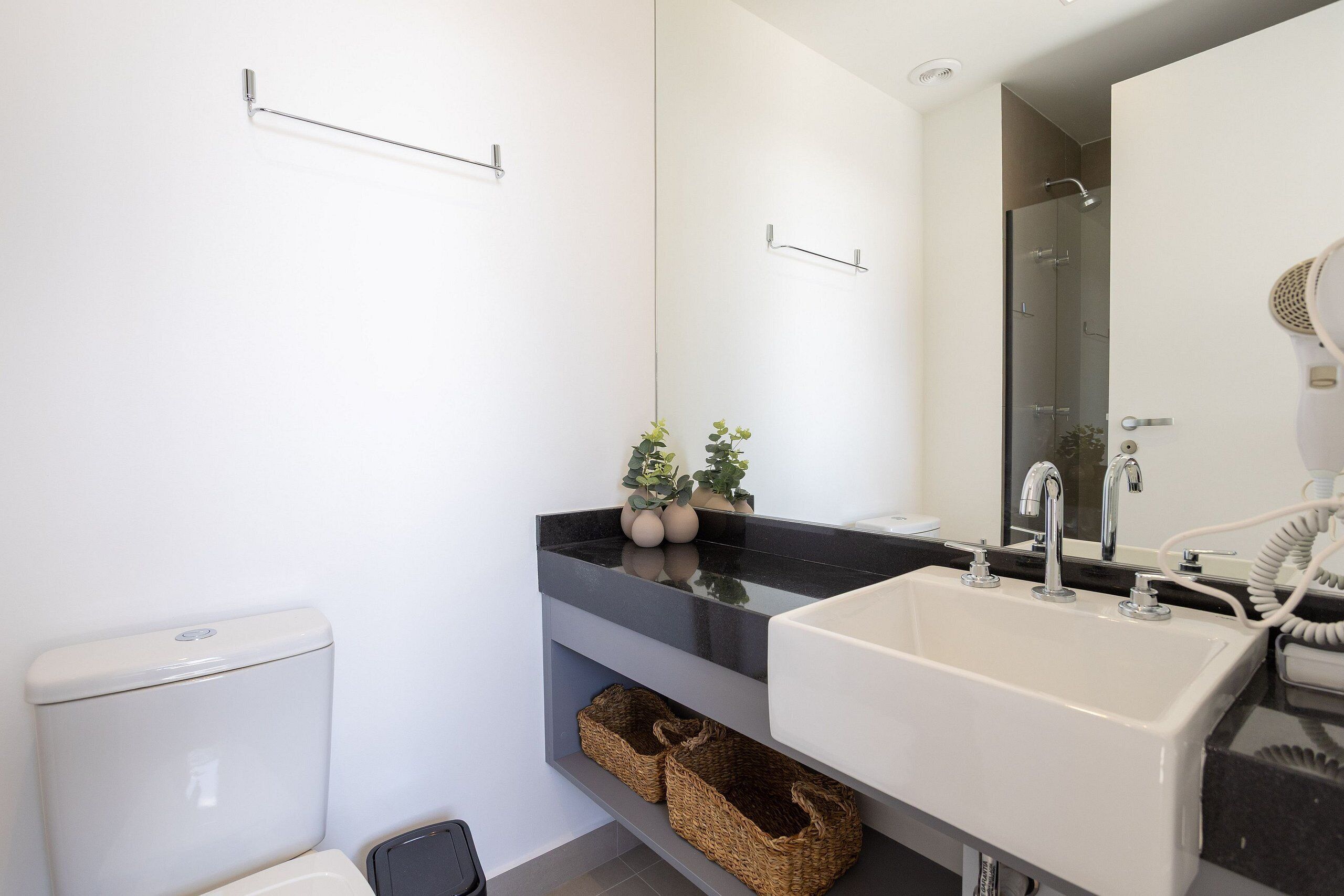 A modern bathroom with a toilet, sink, and shower. There are wicker baskets under the sink and a plant on the countertop.